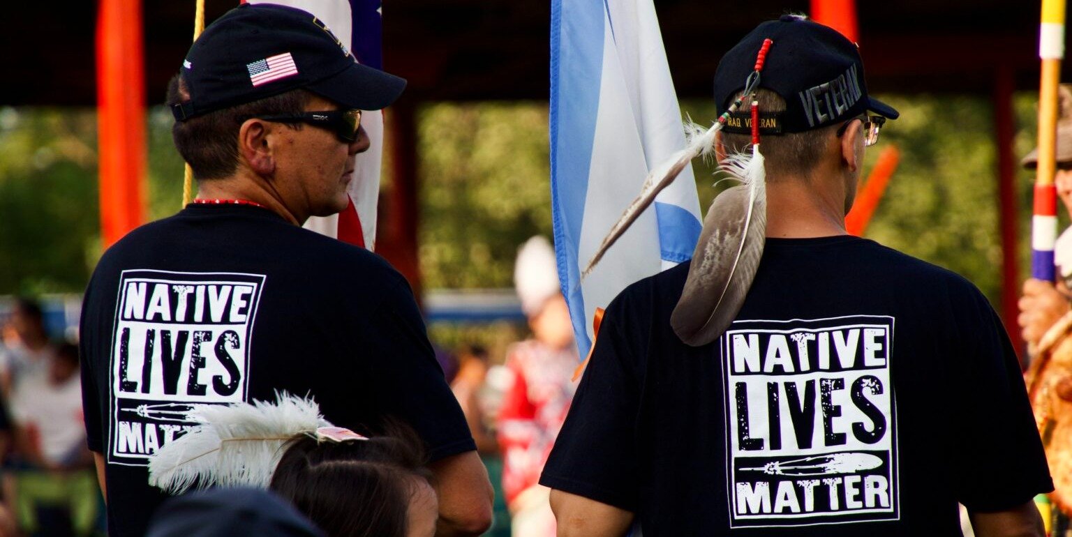 Two adult native american males observing at a Pow Wow.